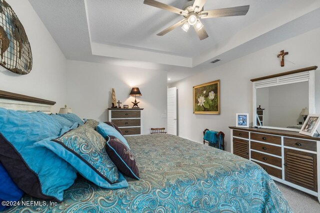 carpeted bedroom with ceiling fan and a raised ceiling