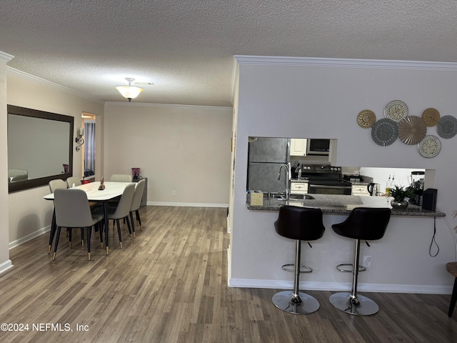 kitchen featuring kitchen peninsula, stainless steel appliances, a textured ceiling, hardwood / wood-style flooring, and ornamental molding