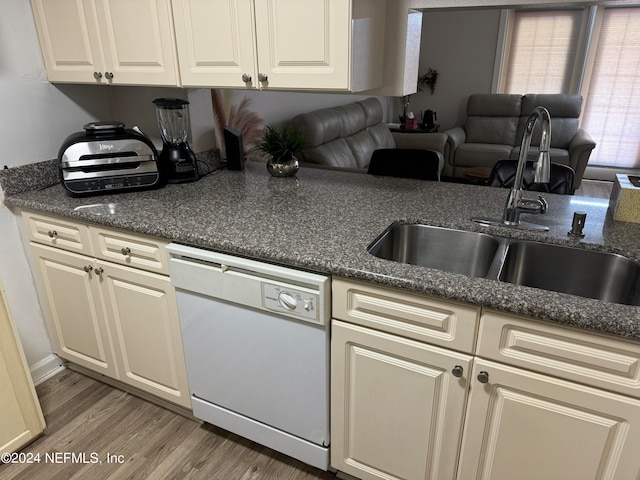 kitchen with cream cabinetry, dishwasher, light wood-type flooring, dark stone counters, and sink