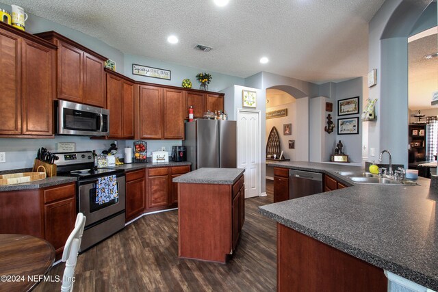 kitchen with appliances with stainless steel finishes, a textured ceiling, kitchen peninsula, and dark wood-type flooring