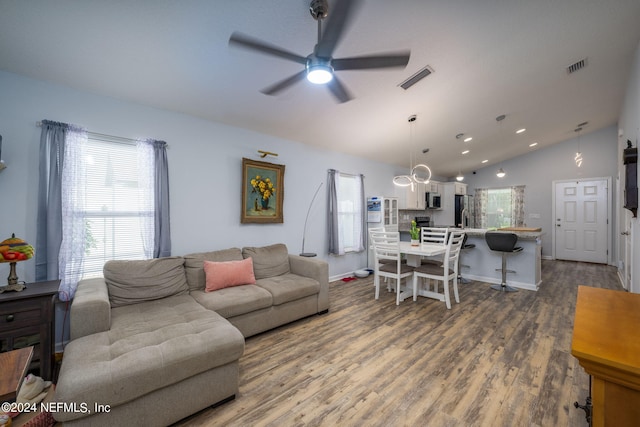 living room with ceiling fan with notable chandelier, vaulted ceiling, and dark hardwood / wood-style flooring