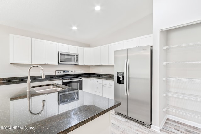 kitchen with appliances with stainless steel finishes, dark stone countertops, vaulted ceiling, white cabinetry, and sink