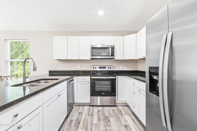 kitchen featuring sink, dark stone counters, white cabinetry, stainless steel appliances, and light wood-type flooring