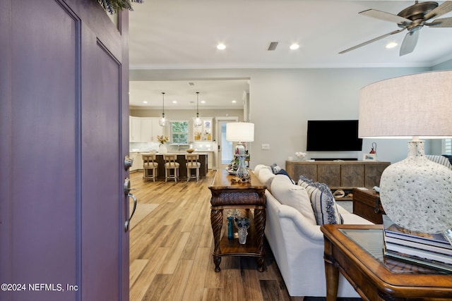 living room with light hardwood / wood-style floors, ornamental molding, and ceiling fan