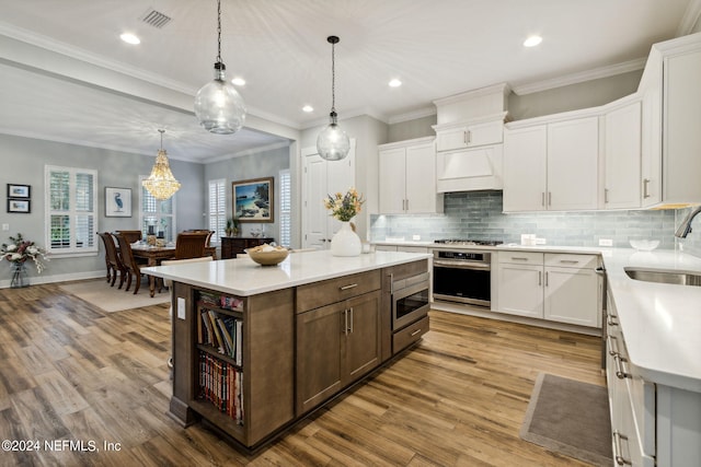 kitchen featuring light wood-type flooring, white cabinets, a kitchen island, stainless steel appliances, and ornamental molding