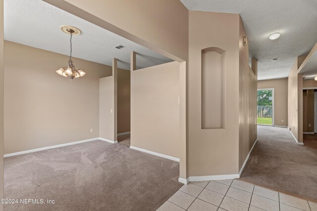 corridor with light carpet, a textured ceiling, and a notable chandelier