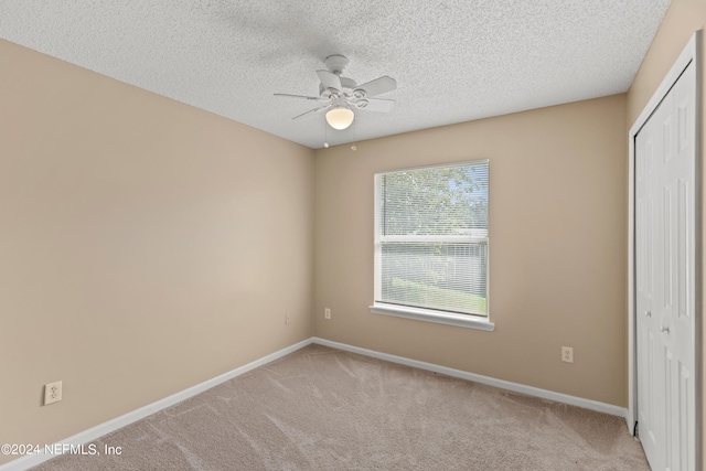 unfurnished bedroom with ceiling fan, a textured ceiling, a closet, and light carpet