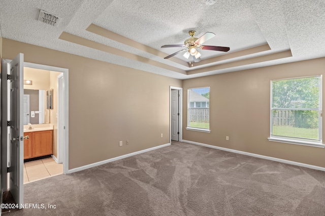 unfurnished bedroom with light carpet, a tray ceiling, ceiling fan, and ensuite bath