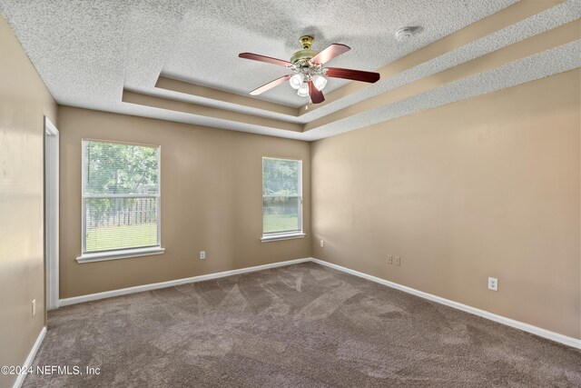 unfurnished room featuring ceiling fan, carpet floors, a tray ceiling, and plenty of natural light