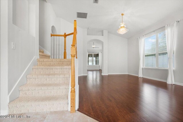 stairway with wood-type flooring, a notable chandelier, and vaulted ceiling