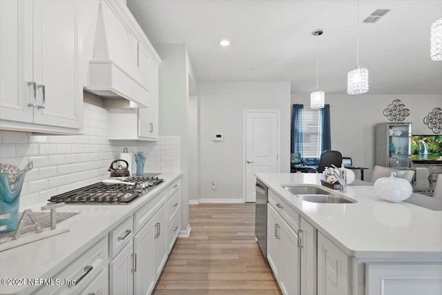 kitchen featuring custom range hood, light hardwood / wood-style floors, an island with sink, white cabinets, and sink