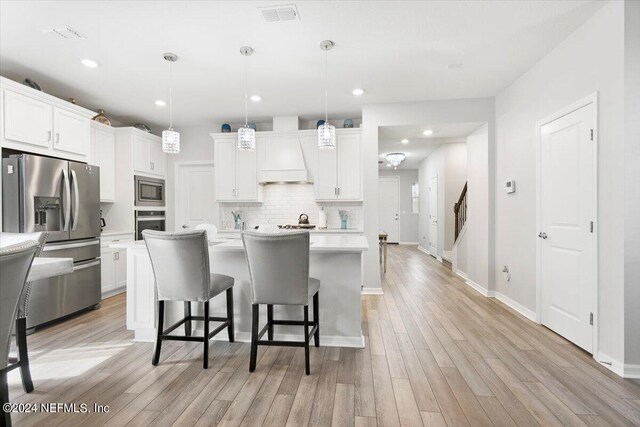 kitchen featuring pendant lighting, white cabinetry, appliances with stainless steel finishes, and light hardwood / wood-style flooring