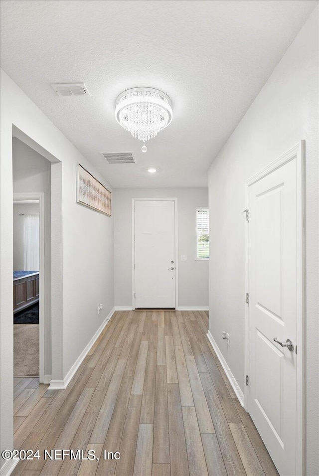 foyer entrance with a textured ceiling, light hardwood / wood-style floors, and a notable chandelier