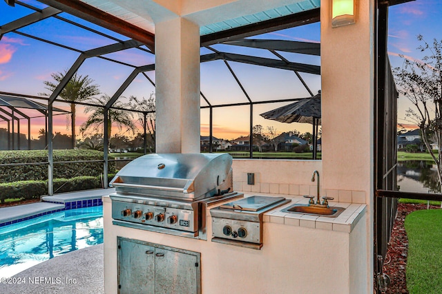 patio terrace at dusk featuring area for grilling, grilling area, sink, a water view, and glass enclosure