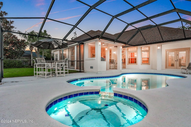 pool at dusk with ceiling fan, glass enclosure, a patio, french doors, and an in ground hot tub