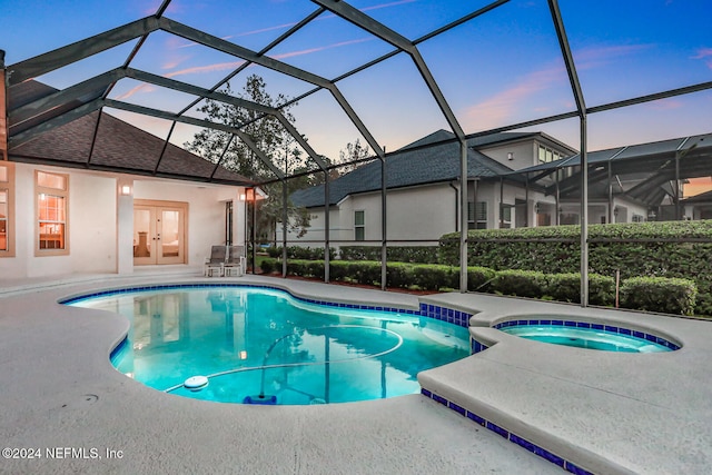 pool at dusk featuring an in ground hot tub, a patio, and glass enclosure