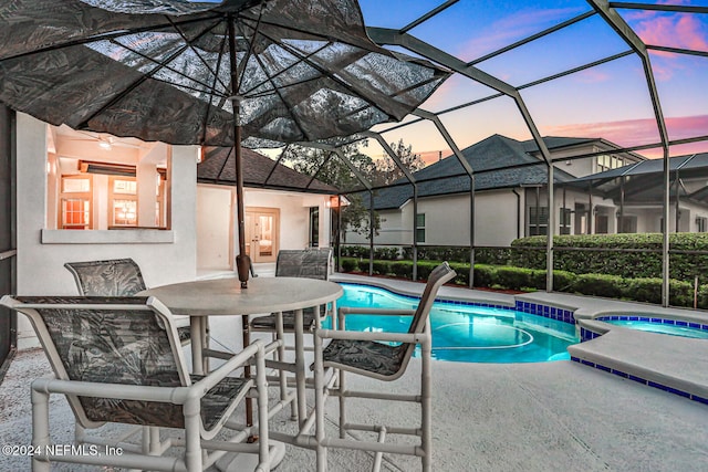 pool at dusk with a patio area, a lanai, and an in ground hot tub