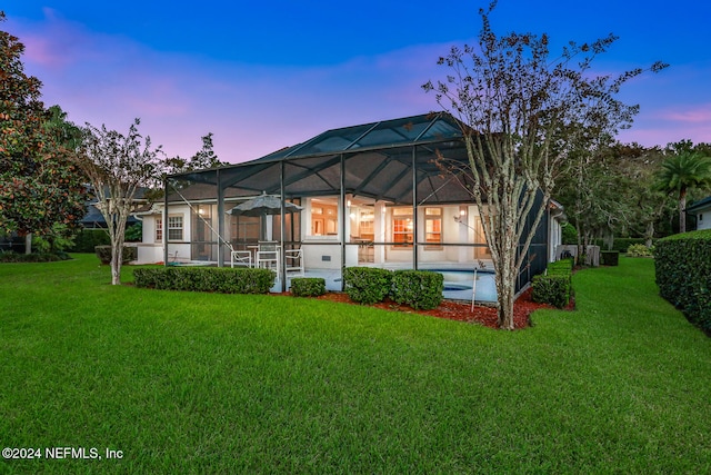 back house at dusk featuring a yard, a patio area, and glass enclosure