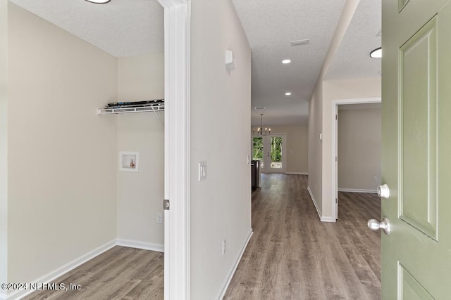 corridor with a chandelier, light hardwood / wood-style floors, and a textured ceiling