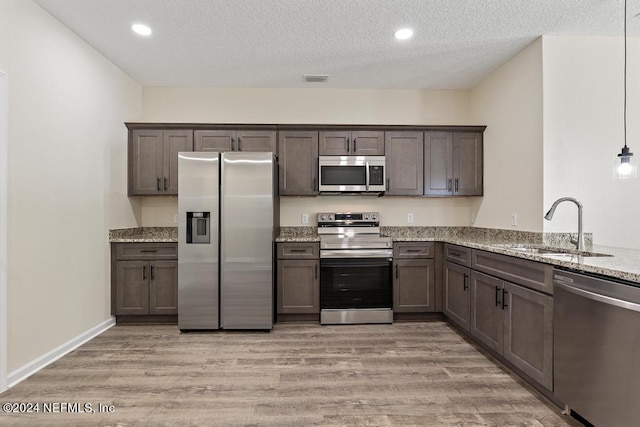 kitchen with hanging light fixtures, sink, light hardwood / wood-style flooring, appliances with stainless steel finishes, and light stone countertops