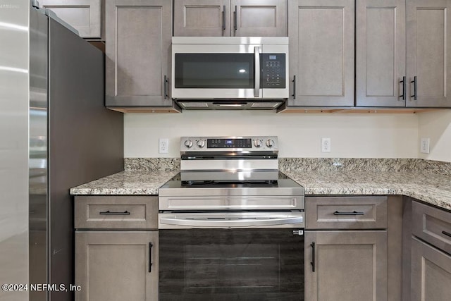 kitchen featuring gray cabinetry, light stone counters, and appliances with stainless steel finishes