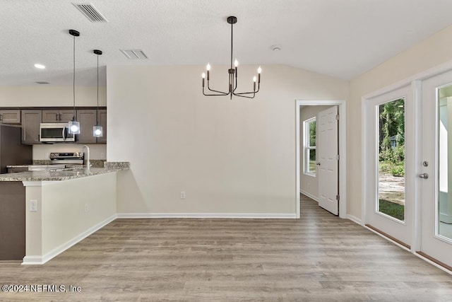 kitchen featuring light hardwood / wood-style floors, lofted ceiling, appliances with stainless steel finishes, decorative light fixtures, and light stone countertops