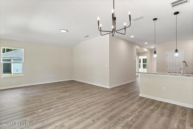 unfurnished living room with a textured ceiling, a chandelier, and hardwood / wood-style floors