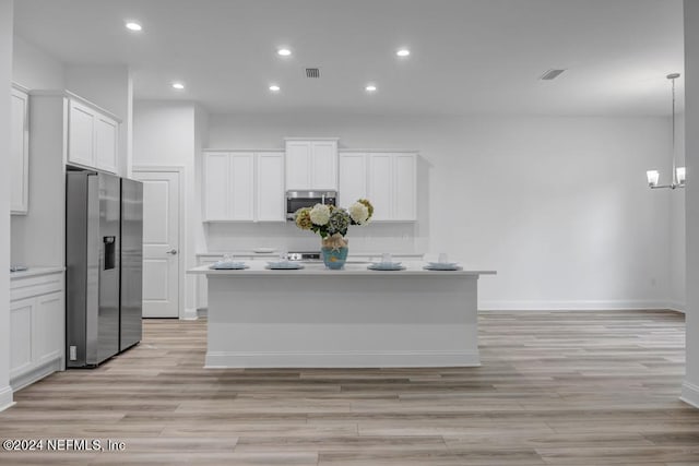 kitchen featuring an island with sink, stainless steel appliances, white cabinetry, and decorative light fixtures