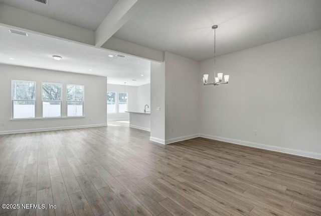 unfurnished room with visible vents, a notable chandelier, baseboards, and wood finished floors