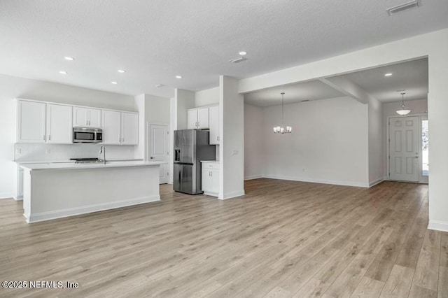 kitchen featuring stainless steel appliances, light countertops, visible vents, open floor plan, and white cabinetry