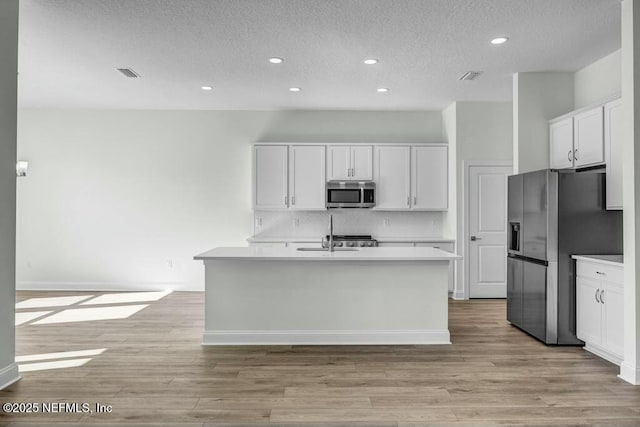 kitchen featuring appliances with stainless steel finishes, white cabinets, light countertops, and an island with sink