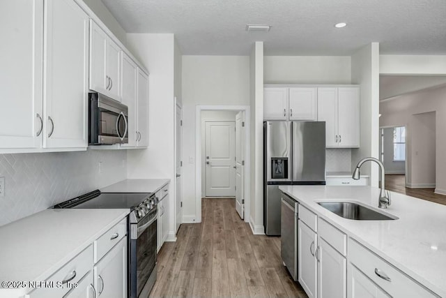 kitchen featuring appliances with stainless steel finishes, a sink, light countertops, white cabinetry, and backsplash