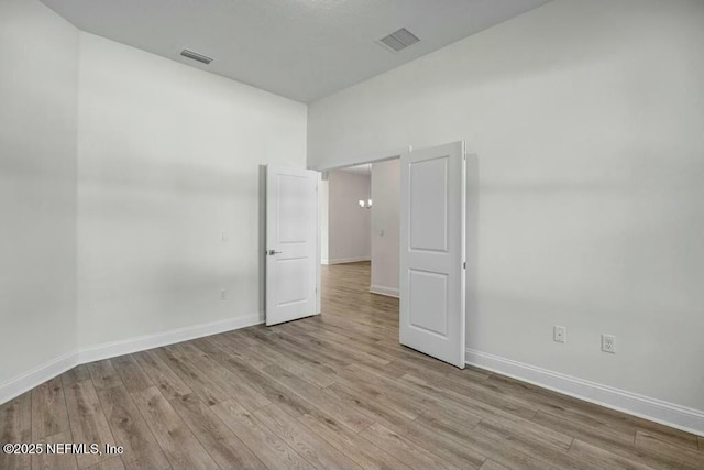 unfurnished room with light wood-type flooring, visible vents, and baseboards