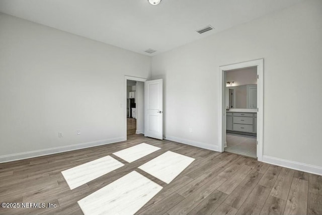 unfurnished bedroom with light wood-style flooring, ensuite bath, visible vents, and baseboards