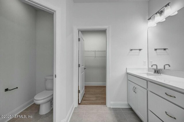 bathroom with toilet, vanity, a walk in closet, and tile patterned floors