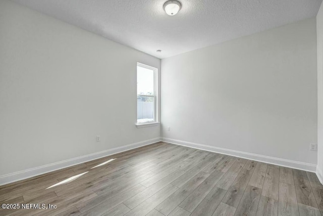 empty room featuring light wood-style flooring, baseboards, and a textured ceiling