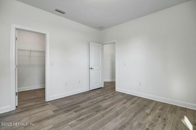 unfurnished bedroom featuring light wood-type flooring, baseboards, a spacious closet, and visible vents