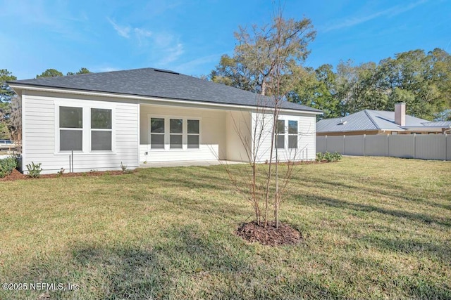 rear view of property with a shingled roof, a lawn, and fence