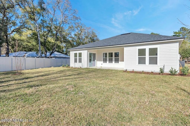 rear view of house with roof with shingles, a lawn, and fence