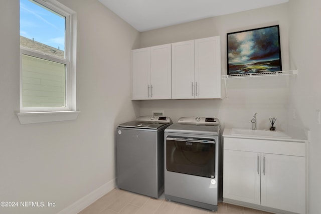 clothes washing area with light hardwood / wood-style floors, separate washer and dryer, sink, and cabinets