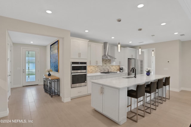 kitchen with a kitchen island with sink, sink, white cabinets, wall chimney exhaust hood, and appliances with stainless steel finishes