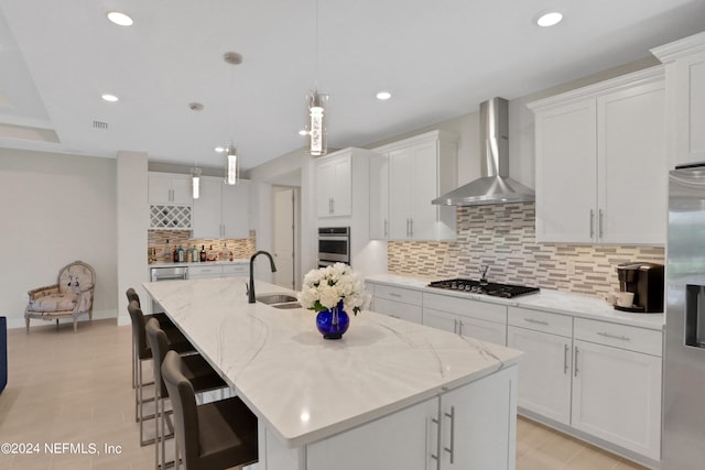 kitchen with white cabinets, a center island with sink, and wall chimney exhaust hood