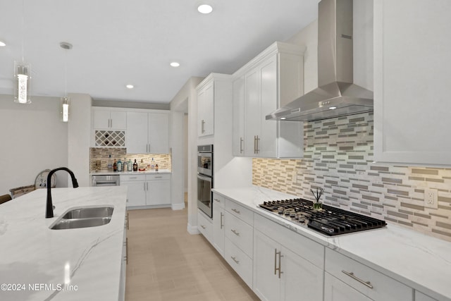 kitchen with sink, wall chimney range hood, white cabinetry, appliances with stainless steel finishes, and light stone countertops