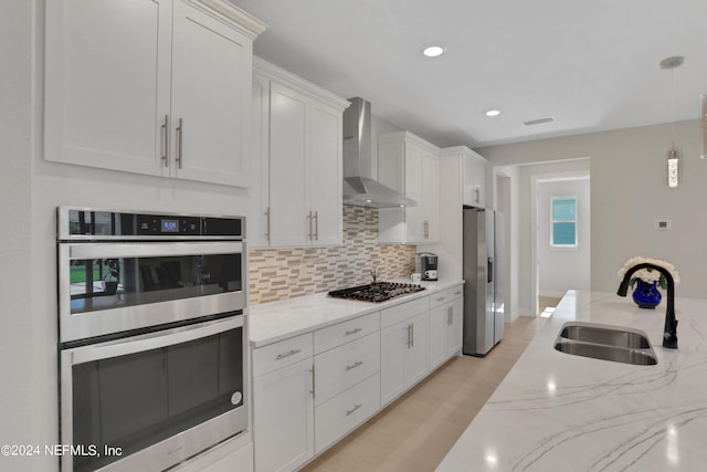 kitchen with appliances with stainless steel finishes, white cabinetry, sink, and wall chimney range hood