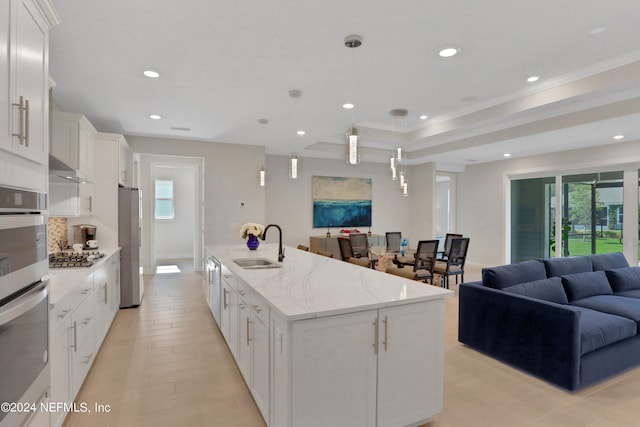 kitchen featuring pendant lighting, a large island with sink, sink, white cabinetry, and appliances with stainless steel finishes