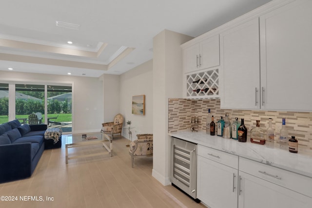 kitchen featuring a raised ceiling, beverage cooler, white cabinetry, light stone countertops, and decorative backsplash