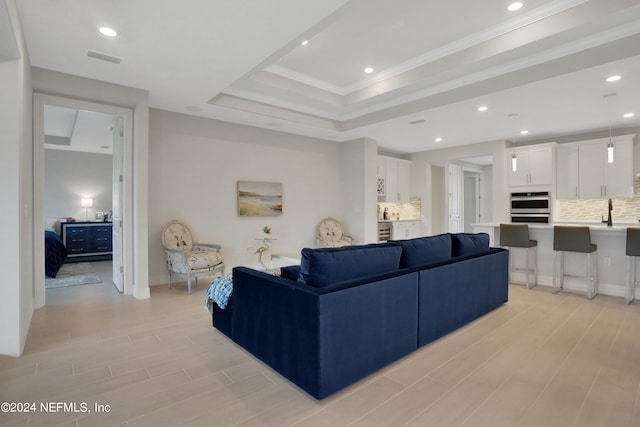 living room featuring light hardwood / wood-style flooring, a raised ceiling, crown molding, and sink