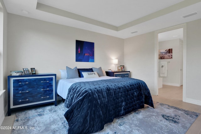 bedroom featuring a raised ceiling, ensuite bathroom, and hardwood / wood-style floors