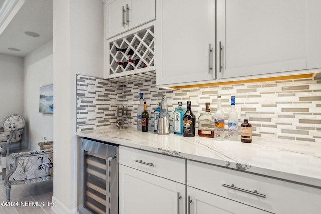 bar with light stone counters, wine cooler, white cabinets, backsplash, and tile patterned floors