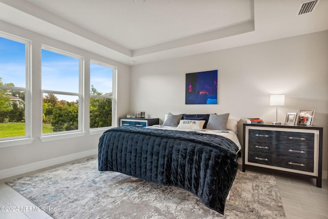 bedroom featuring multiple windows, light hardwood / wood-style floors, and a tray ceiling